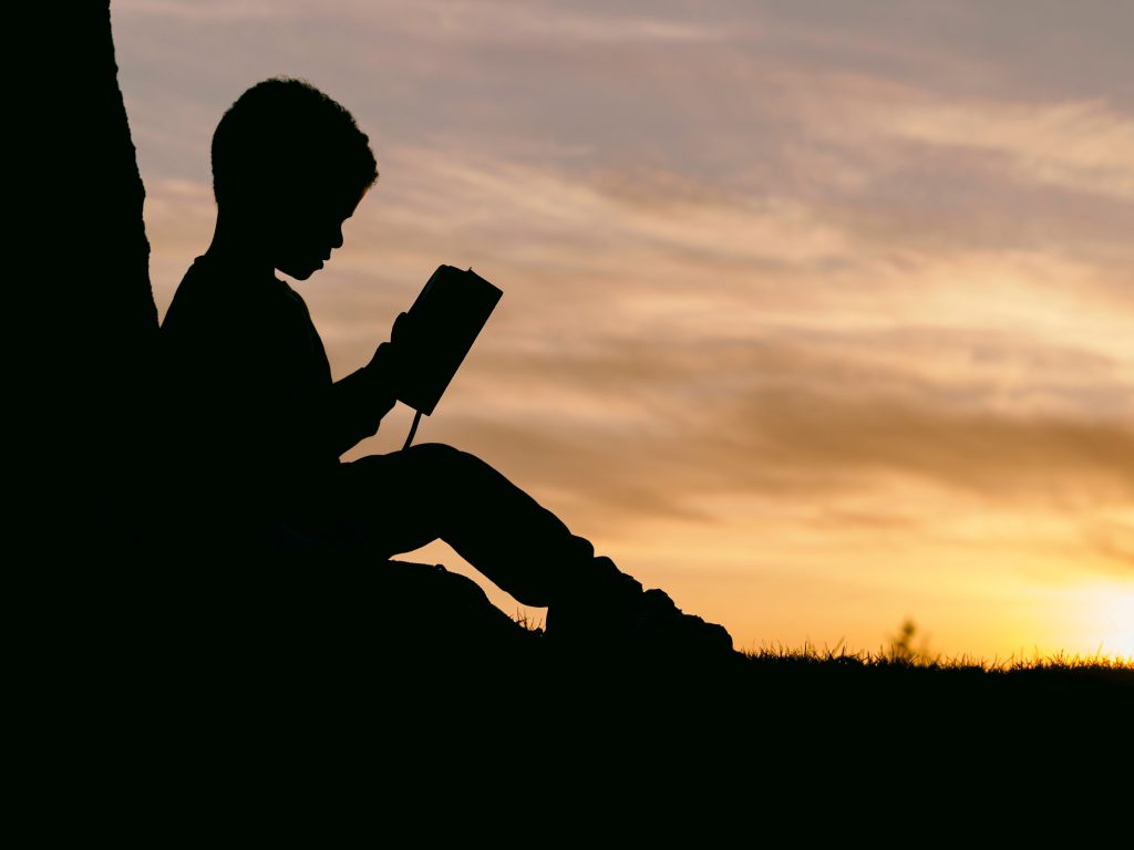 A boy reading by the sunset.
